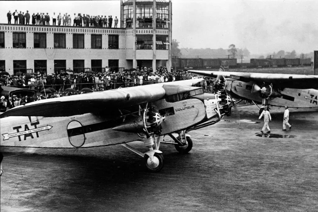 Historic image of John Glenn International Airport with crowd of people and vintage airplanes on the ramp in front of the terminal building
