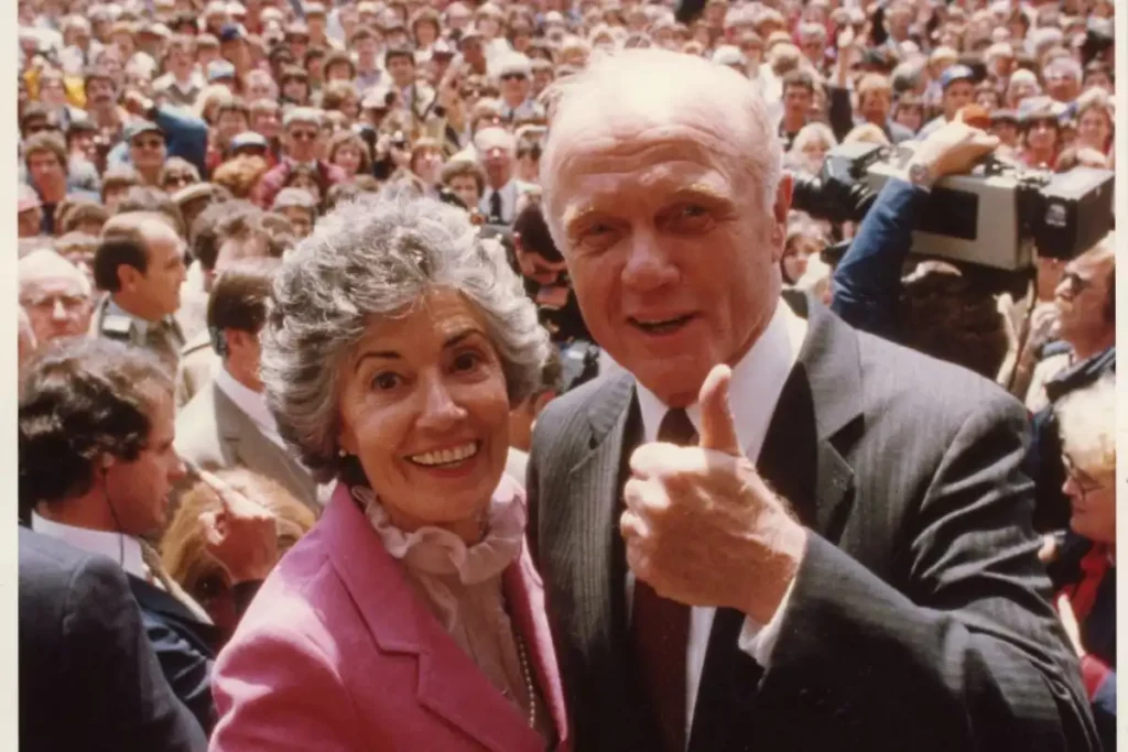 John and Annie Glenn, formally dressed at an event with large crowd of people in the distance.
