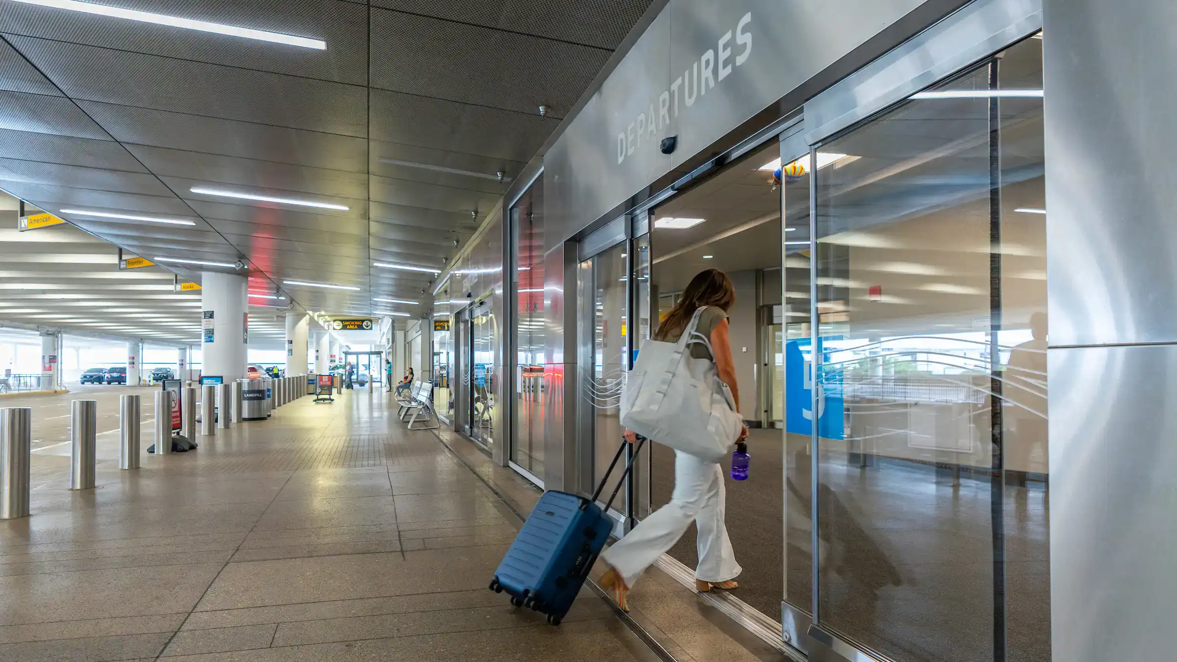 Female passenger pulling a blue suit case from the curb into the departures area at John Glenn International Airport