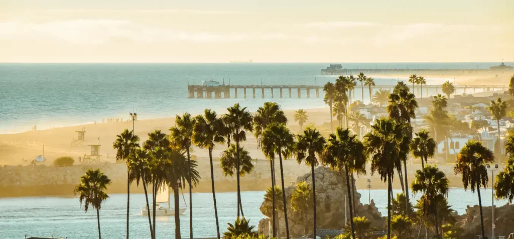 Orange County, California sunny beach with palms and pier in the distance