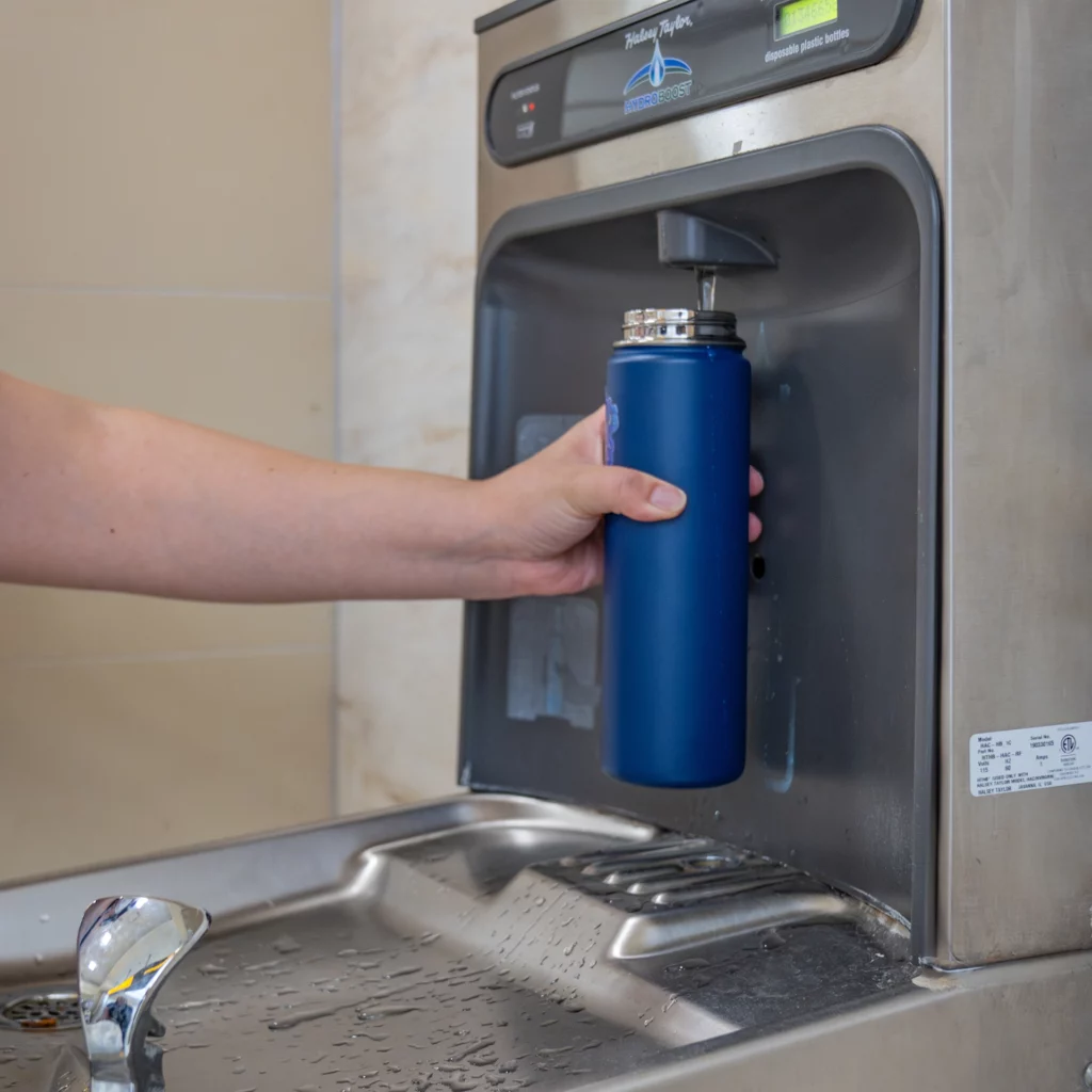 A person using a water fill station at CMH to fill a blue water bottle at John Glenn International