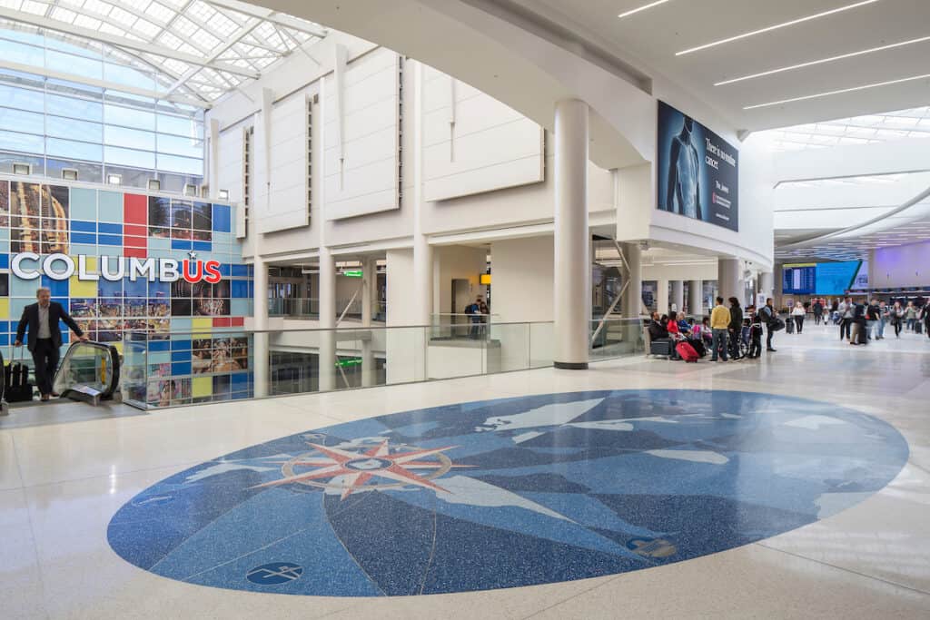 John Glenn International, also known as CMH Airport, is a Columbus airport with a blue floor and people walking around.