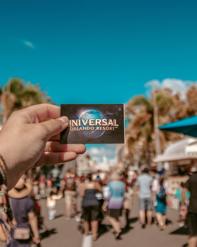 A hand holds up a Universal Studios card against a blue sky and crowd in front of them.