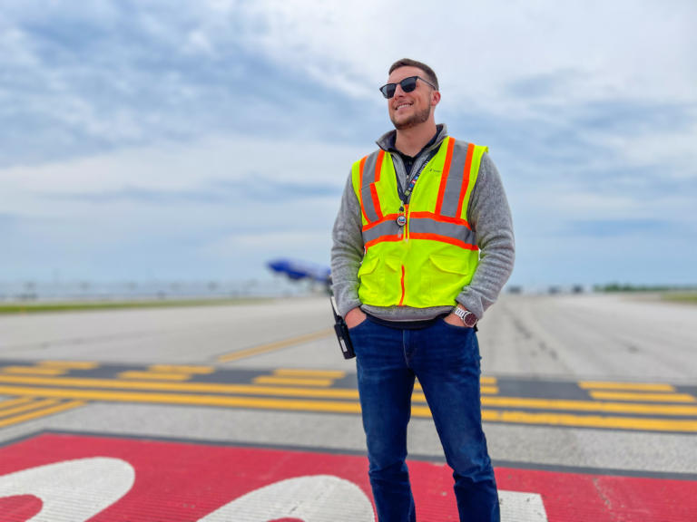 A man in a vest standing on a CRAA airport taxiway.