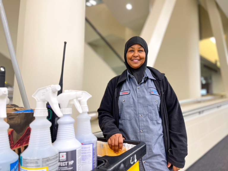 A woman in a hijab standing next to a cart of cleaning supplies at Columbus Regional Airport Authority.