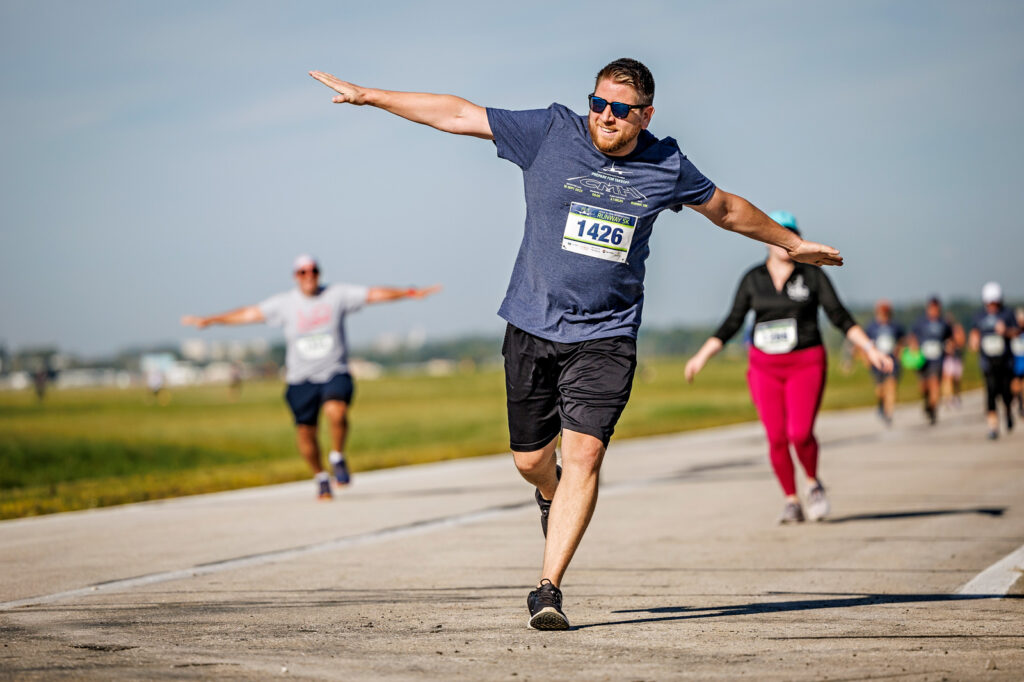 A runner stretches his arms out to replicate an airplane as he runs into the finish line of a 5K.