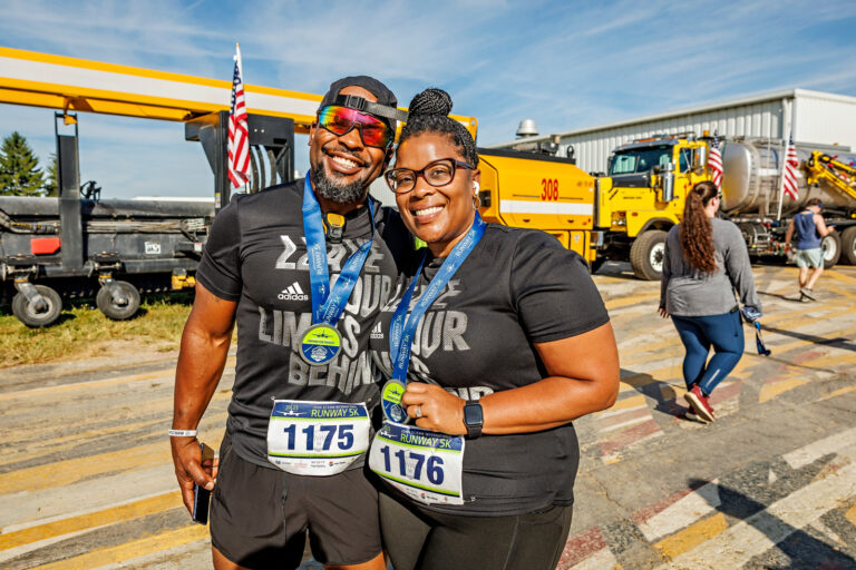 Two racers pose together with their medals after completing the 5K at the airport.