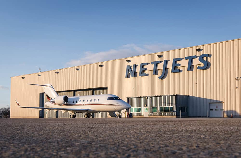 A corporate plane is parking outside of NetJets on the ramp during golden hour.