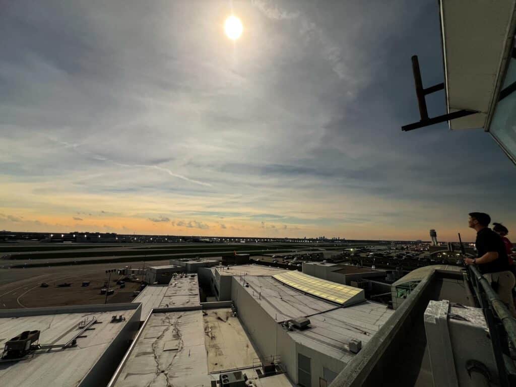 Two employees stand on the catwalk outside of an old air traffic control tower, looking up at the Solar Eclipse as the moon passes in front of the sun.