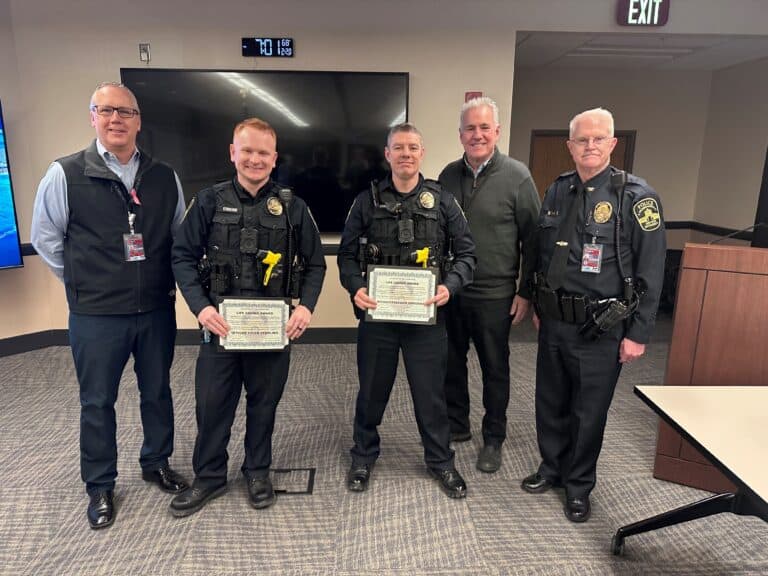 Two police officers holding commendation certificates stand flanked by three other individuals in a conference room.