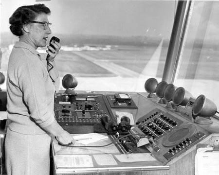 An air traffic controller using a microphone and monitoring equipment at an airport control tower.