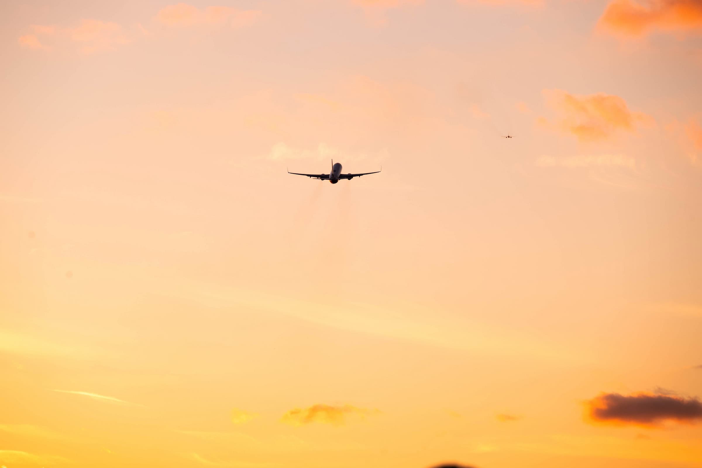 An airplane flying towards the horizon under a vibrant sunset sky.