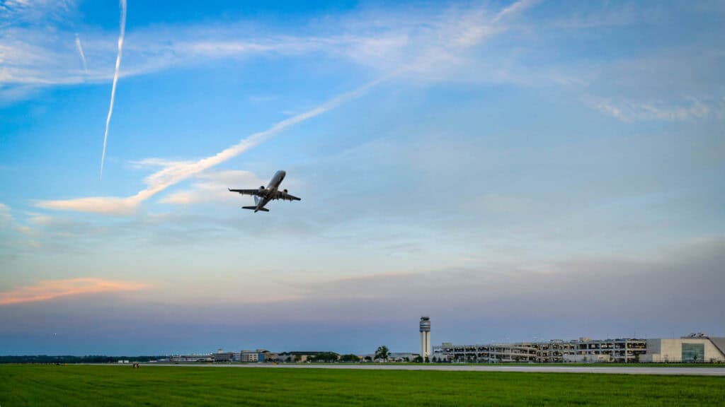 An airplane taking off from an airport at sunrise, with a clear blue sky and contrails visible overhead.