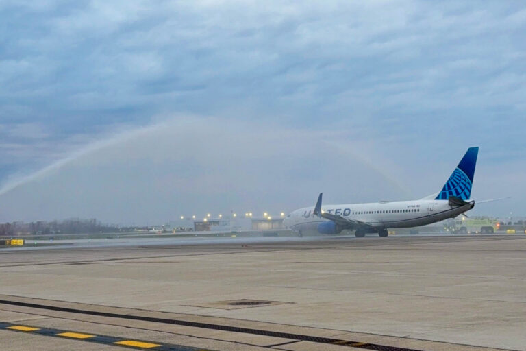 A United Boeing 737-900 taxis under a water arch created by two airport firefighting trucks.