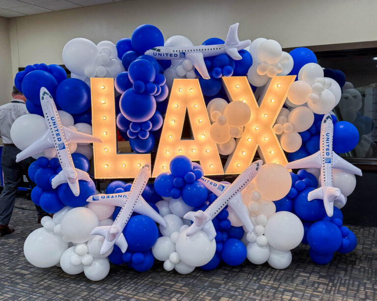 A large balloon display with white and blue balloons, and plane balloons that have United's logo on them. In the middle are three large lit up letters spelling out LAX.