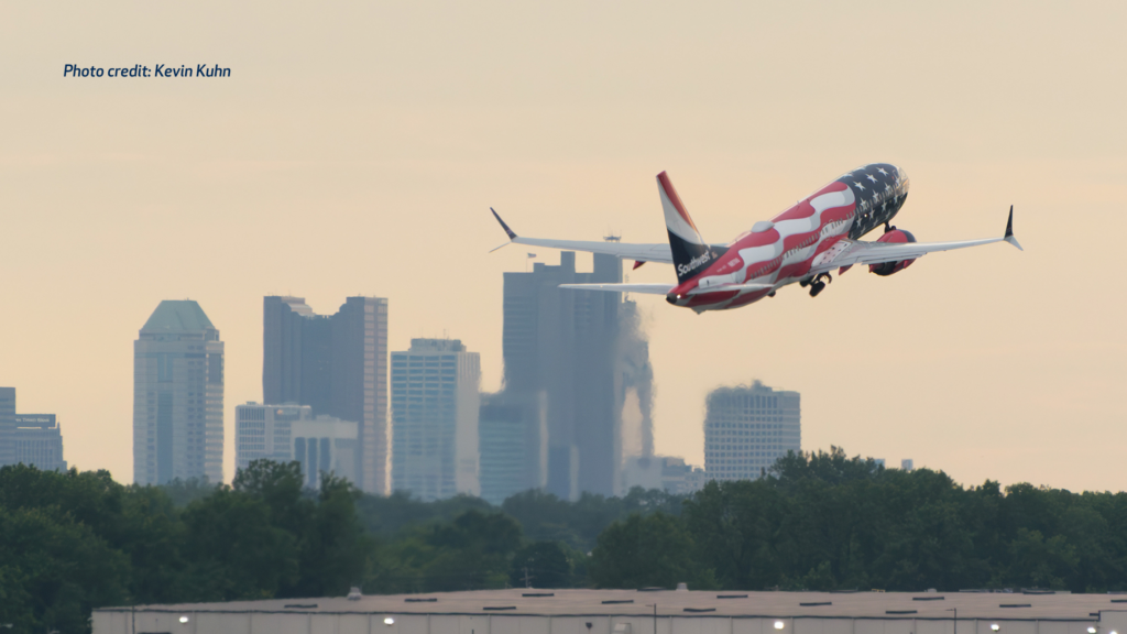 Southwest Airlines plane in a red, white and blue American flag livery taking off at dusk, with the Columbus skyline visible in the background.