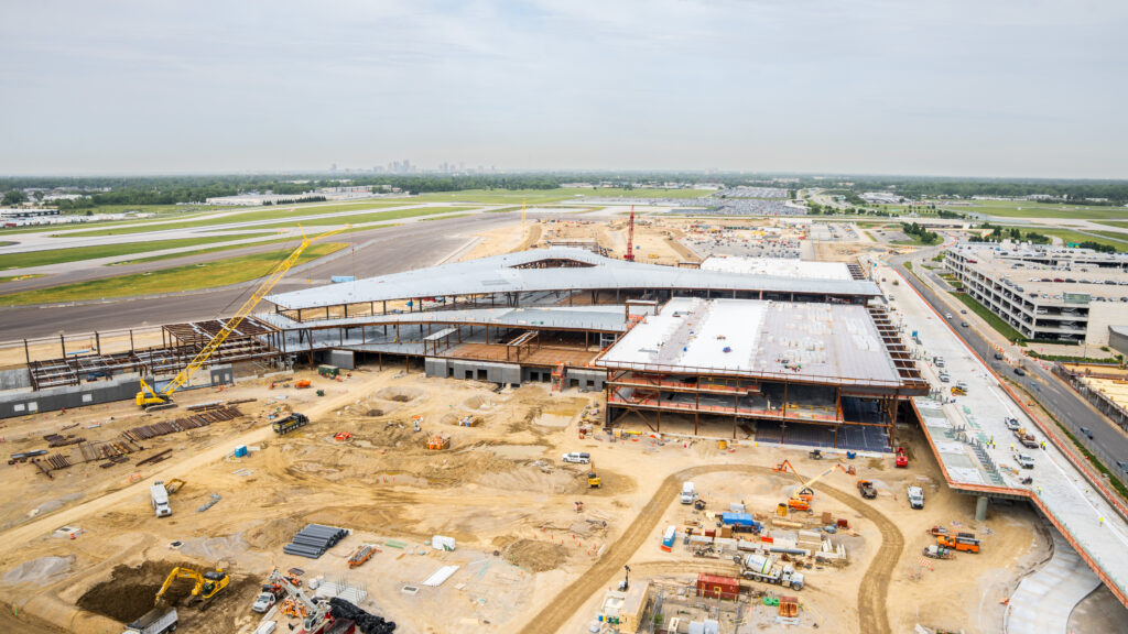 Aerial view of construction on the new terminal at John Glenn Columbus International Airport, showing the terminal structure, elevated roadway, cranes, construction equipment, and surrounding runways.
