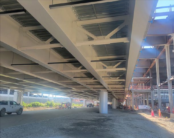 Aerial view of CMH Next construction at John Glenn Columbus International Airport, showing the elevated roadway, new terminal and parking structures, construction cranes, equipment, and surrounding airport grounds.