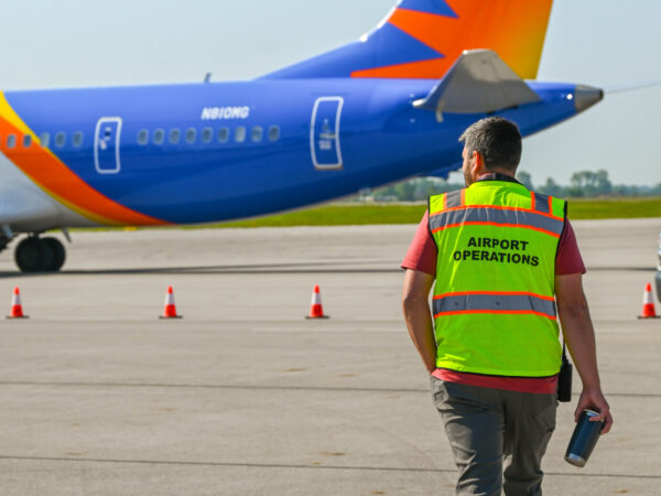 Airport operations worker on runway, walking towards Allegiant airplane.